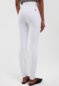 Vaqueros skinny de denim blanco con cintura alta, que cuentan con dos bolsillos traseros y una pequeña etiqueta de logo roja en la cinturilla. Tejido texturizado, ajuste elegante.