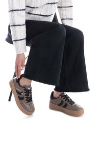 Zapatos deportivos marrones y negros con una textura suave, suela de goma y cordones negros. Llevados con pantalones anchos negros y un suéter blanco a rayas.