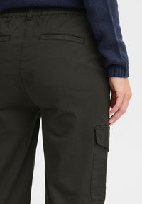 Donkergroene cargobroek met een elastische tailleband, twee achterzakken en details aan de zijzakken. Het materiaal lijkt glad met een matte afwerking.