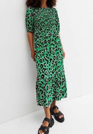 Grön leopardmönstrad klänning med smockat liv och korta puffärmar, med en flätad kjol. Kombineras med kraftiga svarta sandaler.