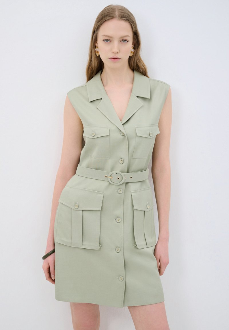 Robe sans manches verte avec col, fermeture à boutons, poches avant et taille ceinturée. Fabriquée en tissu texturé, avec une coupe ajustée.