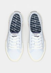 Balti zemas virsmas sneakeri ar baltiem aukliņām un Pepe Jeans logotipu uz mēles un zolēm ar zīmola rakstu, skatīti no augšas.