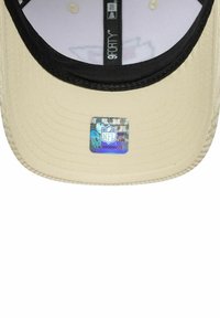 Beige Mütze mit einem schwarzen Schild und genähten Details. Auf der Vorderseite befindet sich ein holographischer NFL-Logo-Aufkleber. Innenfutter ist weiß.