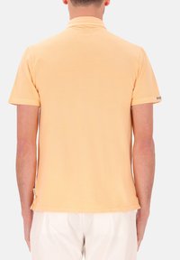 Korte mouwen polo shirt in zacht perzikkleurige stof, met een klassieke kraag, zijsplitten en minimale details aan de zoom en de mouwen.