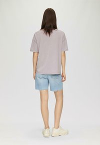 T-shirt oversized violet clair, à manches courtes, associée à un short en denim bleu clair, avec un ourlet effiloché, et des baskets couleur crème.