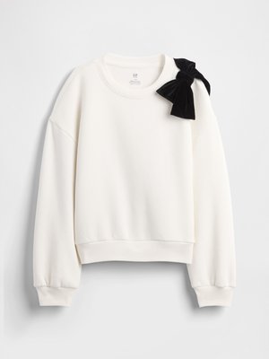 Bluză albă cu mâneci lungi, cu manșete și tiv côtelés, având un mare papion negru din catifea pe umărul stâng.