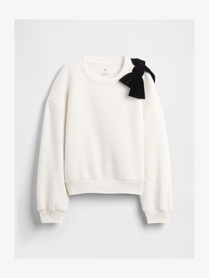 Fehér hosszú ujjú pulóver bordázott mandzsettával és szegéllyel, nagy fekete bársony masnival a bal vállnál.