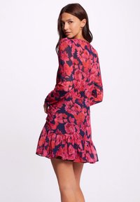 Floral dress featuring a navy base with vibrant pink flowers, long sleeves, ruffled hem, and a fitted silhouette. Made of lightweight fabric.