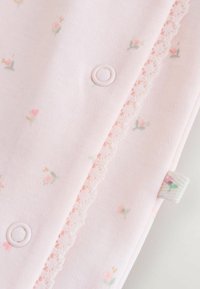 Rosa tyg med blommönster som innehåller små rosor. Tygstycket har en spetskant och en plastknäppe för stängning.