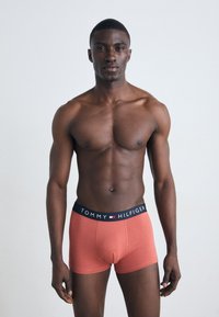 Piros boxer alsónemű fekete derékkal, amelyen a "TOMMY HILFIGER" felirat látható. Az anyag simának tűnik, szorosan illeszkedik a test formájához.