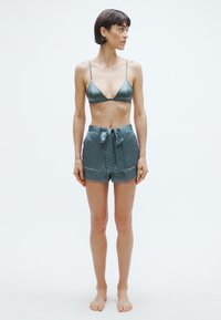 Zöld szatén háromszög melltartó és mintás rövidnadrág, megkötős derékkal. A ruházat sima textúrájú, a rövidnadrág pedig geometrikus mintázatú.