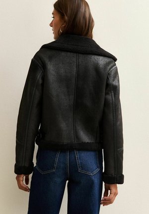 Zwarte schapenvachtjas met een kraag, manchetmouwen en een ceintuur in de taille. Geweven leren afwerking, cropped ontwerp en zichtbare stiksels.