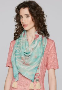 Lightweight, semi-sheer scarf in aqua with abstract floral patterns and cream tassels at the ends, draped around the neck.