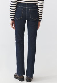 Jeans svasati in denim scuro con vita regular, cuciture a vista e due tasche posteriori. Abbinati a scarpe marroni e un maglione a righe.