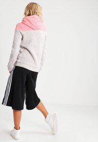 Grijs en roze kleurgeblokte hoodie met capuchon, gecombineerd met zwarte shorts met witte strepen aan de zijkanten en witte sneakers.