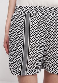 Černobílé šortky s geometrickým vzorem, elastickým pasem a bočním pruhem. Materiál vypadá lehký a texturovaný.