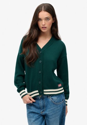 Gilet tricoté vert avec un décolleté en V, fermeture à boutons, et des poignets et un ourlet à rayures blanches. Doté d'un petit emblème près du bas.