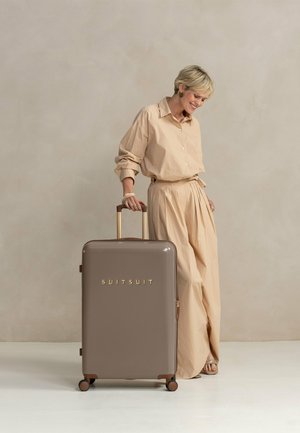 Hard-shell suitcase in matte brown, features gold text "SUITSUIT," sturdy wheels, and a retractable handle. Smooth finish, rectangular shape.
