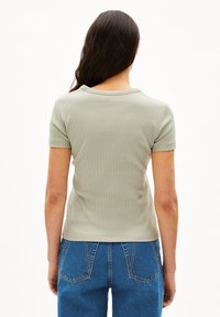 Světlé zelené žebrované tričko s krátkými rukávy a kulatým výstřihem. Kombinováno s modrými džínami s vysokým pasem.