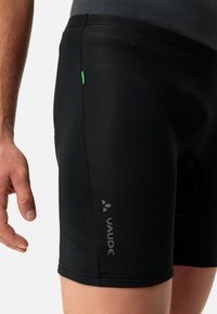 Pantaloni ciclistici neri con una vestibilità aderente, materiale elastico e un'etichetta accentata in verde. Presentano il logo "VAUDE" in grigio sul lato sinistro.