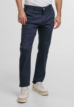 Marineblauwe chinos met een recht model, gemaakt van zachte stof. Voorzien van een knoopsluiting en zijzakken. Draagt men met beige en witte sneakers.