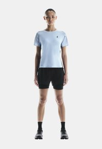 T-shirt de sport bleu clair à manches courtes, avec une texture subtile et un logo. Associé à un short noir et des chaussures de course.