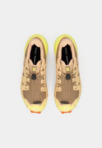 Αθλητικά παπούτσια σε καφέ και μπεζ με πάνω μέρος από δίχτυ, κίτρινες λεπτομέρειες, σύστημα γρήγορου δέσιμου και ανάγλυφες σόλες σε πορτοκαλί και μαύρο.