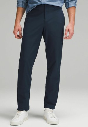 Marineblå slim-fit bukser lavet af letvægtsstof, med flad front og sidelommer, parret med hvide sneakers.