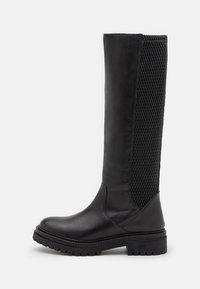 Bota negra hasta la rodilla con material de cuero suave, panel de malla texturizada, suela de goma duradera y detalles de costura reforzada.