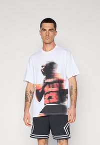 White cotton t-shirt featuring a colorful, blurred graphic of a basketball player and the number "23" on the front. Paired with black perforated shorts.