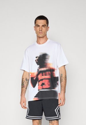 Tricou alb din bumbac, având un grafic colorat și neclar al unui jucător de baschet și numărul "23" pe față. Asortat cu pantaloni scurți negri perforați.