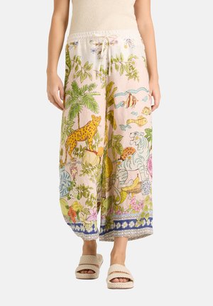 Wijde broek met kleurrijke tropische prints van een luipaard, witte tijger, vis, planten en bloemen, gedragen met beige sandalen.