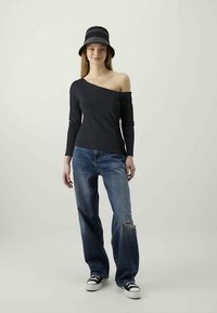 Top preto à parte dos ombros com mangas longas, combinado com jeans azuis rasgados e ténis pretos de cano baixo. Chapéu de balde preto riscado.