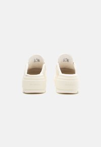 Kremfargede slip-on sneakers med et teksturert stoffoverdel og polstret krage; har preget "AIR JORDAN" merking på hælen.