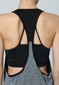 Svart sportbh med racerback-design, lagd under en grå linne med utskurna sidor och en texturerad tyg.