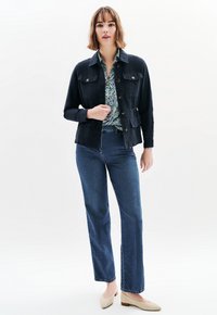 Tummansininen, istuva takki, jossa on kaksi rintataskua ja nappikiinnitys, käytetään kukkapaidan päällä. Yhdistetty korkeavyötäröisiin sinisiin farkkuihin ja beigeihin loafer-kenkiin.