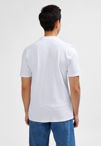 Wit katoenen T-shirt met korte mouwen en een ronde hals, gecombineerd met lichtblauwe denim jeans, gezien vanaf de achterkant.