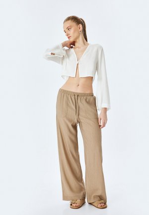 Witte gecropt lange mouwen top met een knoopdetail aan de voorkant, gecombineerd met beige wijde broek met een textuurafwerking en een elastische tailleband.