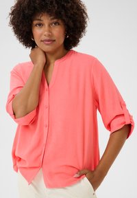 Camicia button-up corallo con scollatura a V e maniche arrotolabili. Realizzata in tessuto morbido, presenta una vestibilità ampia e un orlo curvato per il massimo comfort.