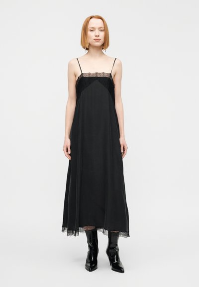 Μαύρο μακρύ φόρεμα με δαντελένια διακόσμηση στο ντεκολτέ και το τελείωμα. Διαθέτει λεπτές τιράντες και αέρινη σιλουέτα, συνδυασμένο με μαύρες μπότες μέχρι το γόνατο.