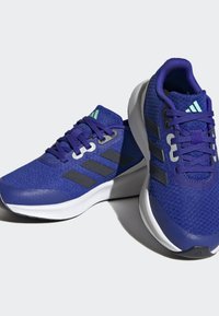 Scarpe sportive viola con tomaia in rete, strisce grigie, suole bianche e dettagli testurizzati. Presenti lacci e accenti riflettenti.
