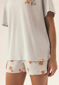 Zestaw loungewear z bawełny, składający się z jasnoszarej bluzki z krótkimi rękawami oraz spodenek w kolorze białym z nadrukiem brzoskwiniowym, z małym detalem w postaci metki w kształcie brzoskwini.