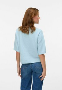 Ljusblå kortärmad tröja med ribbat avslut och mjuk textur, kombinerad med blå högmidjade jeans. Visas bakifrån.