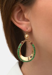 Des boucles d'oreilles créoles dorées présentent un design ouvert, ornées d'accents verts et bordeaux, avec un matériel texturé en haut.