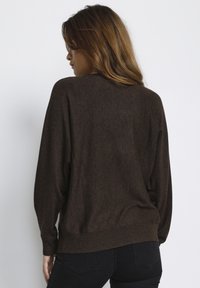 Maglione a maglia marrone con una vestibilità ampia, cuciture delle spalle scese e orlo a coste. La trama appare morbida e leggermente elastica. Modello visto da dietro.