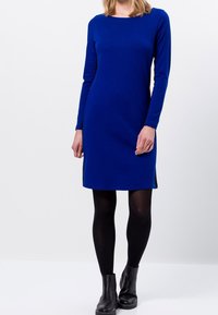 Abito azzurro a maniche lunghe con scollo a giro, tessuto liscio, silhouette aderente, lunghezza al ginocchio, spacchi laterali, abbinato a stivaletti neri alla caviglia.