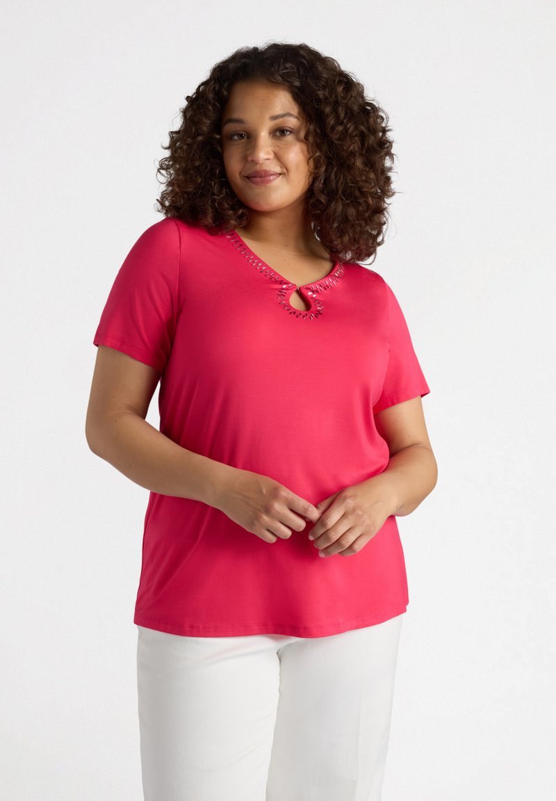 T-shirt rosa a maniche corte in materiale morbido con scollatura a chiave decorata da cuciture decorative. Abbinato a pantaloni bianchi.