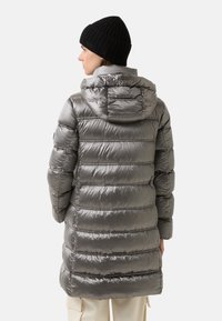 Szara ocieplana parka z kapturem, z poziomą pikowaną teksturą i matowym wykończeniem. Połączona z czapką typu beanie z czarnego ściągacza.