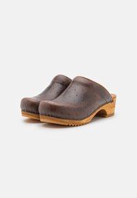 Bruna läderträsko med slät yta, rund tå, träsoffel och strukturerade detaljer. Har en låg klack och synlig sömnad längs kanten.