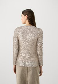 Top beige a maniche lunghe con paillettes, dal design aderente, tessuto testurizzato e dettaglio delle spalle arricciato; abbinato a una gonna beige chiaro.